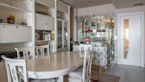 A dining area with a white table and chairs, surrounded by white cabinetry and a glass display cabinet with red items.
