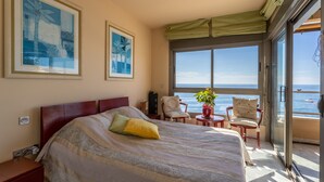 A bedroom with a large bed, a view of the sea, and a balcony with chairs.