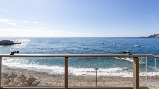A beach view with a railing, ocean, and boats.