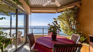 A balcony with a table and chairs, a ceiling fan, and a view of the sea.