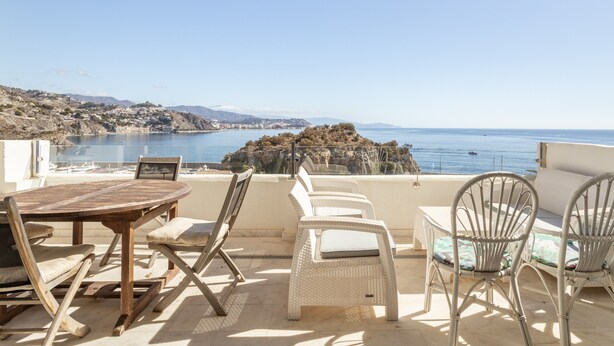 A terrace with a table and chairs, overlooking a coastal landscape with a rocky outcrop. - Vacation Home "Vista Marina" Near the Beach with Sea View, Wi-Fi & Air Conditioning (La Herradura)
