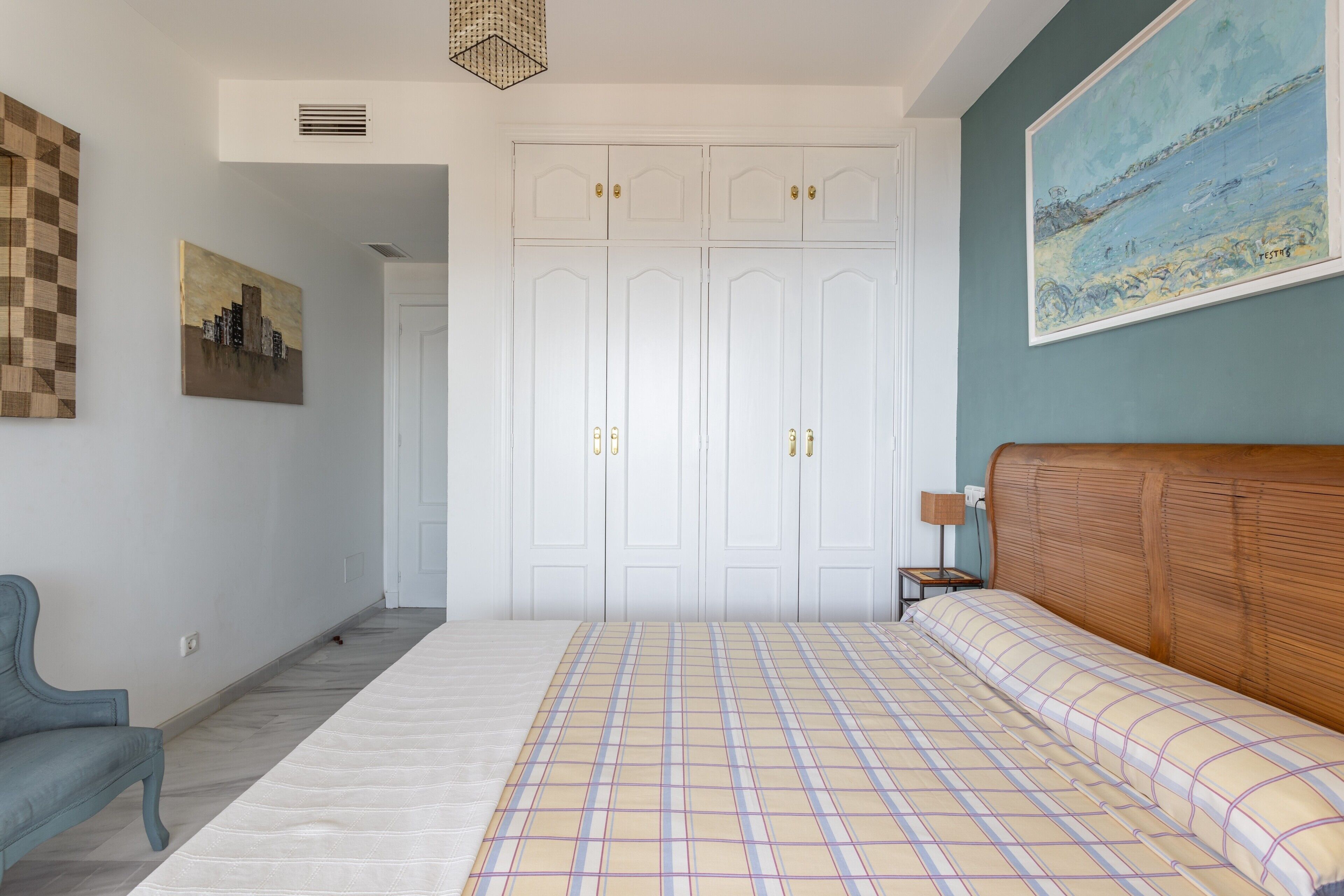 Un dormitorio con cama, armario, una silla y un cuadro en la pared.