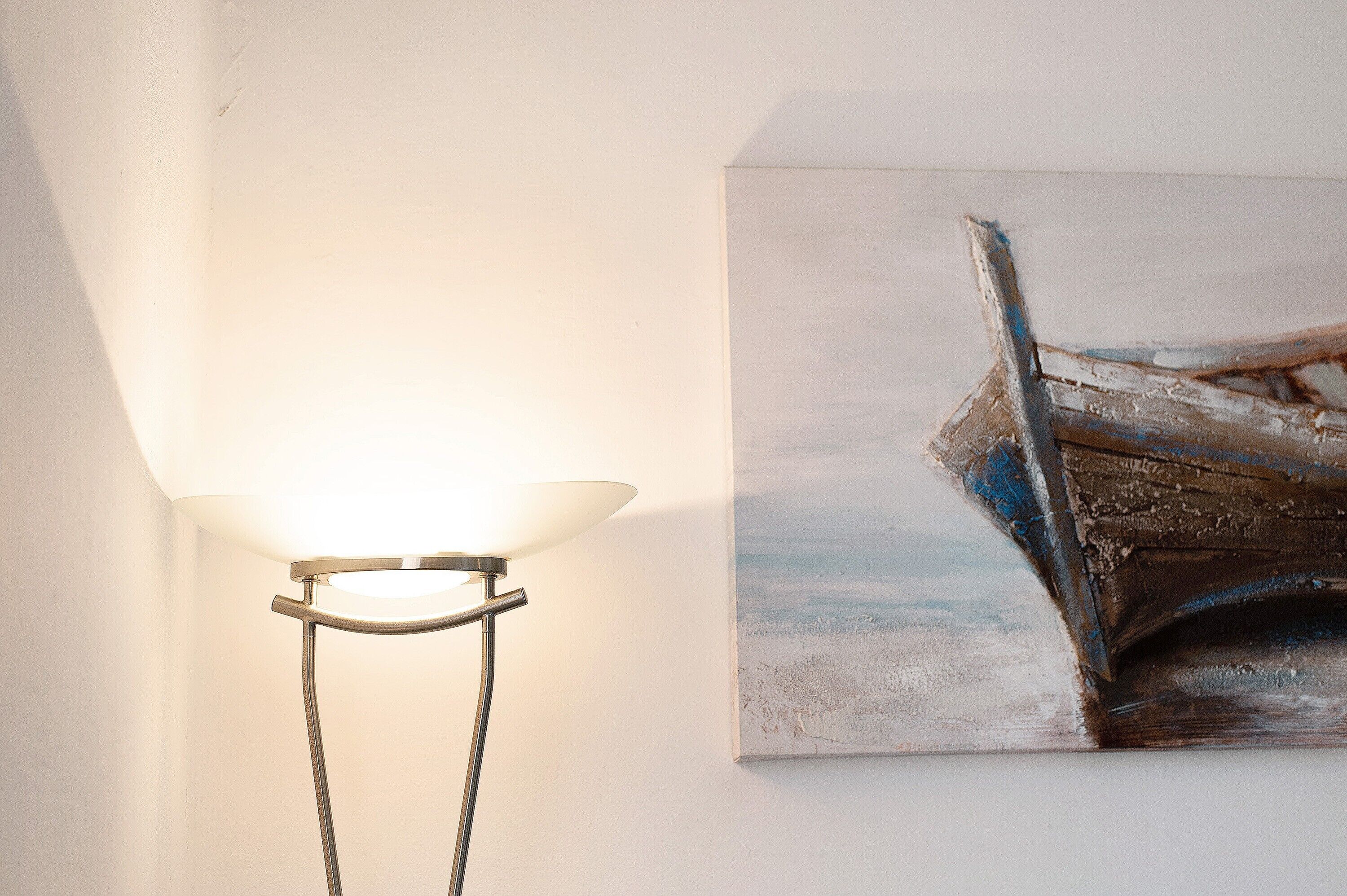 Um candeeiro com cúpula branca e um quadro de um barco na parede.