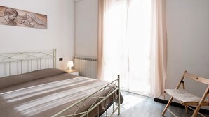 Una camera da letto con un letto, una sedia, una finestra con tende, un termosifone e un'opera d'arte appesa al muro.