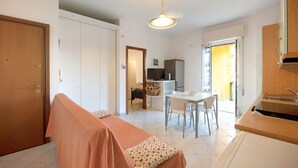 Una habitación con una cama, una mesa de comedor con sillas, un kitchenette y una puerta que da a otra habitación.