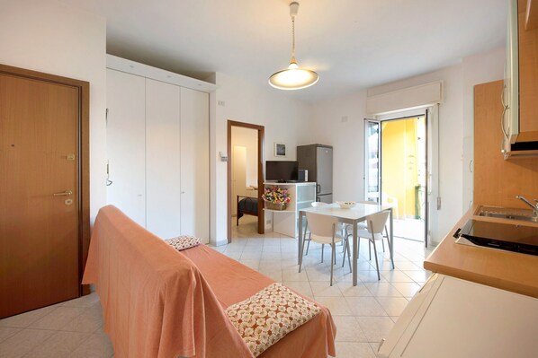 Une pièce comprenant un lit, une table à manger avec des chaises, un coin cuisine et une porte donnant sur une autre pièce.