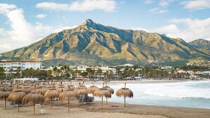 A beach with thatched umbrellas, a mountain in the background, and buildings along the shore. - Villa 'Scandinavian Design' with Sea View, Wi-Fi and Air Conditioning (Puerto Banús)