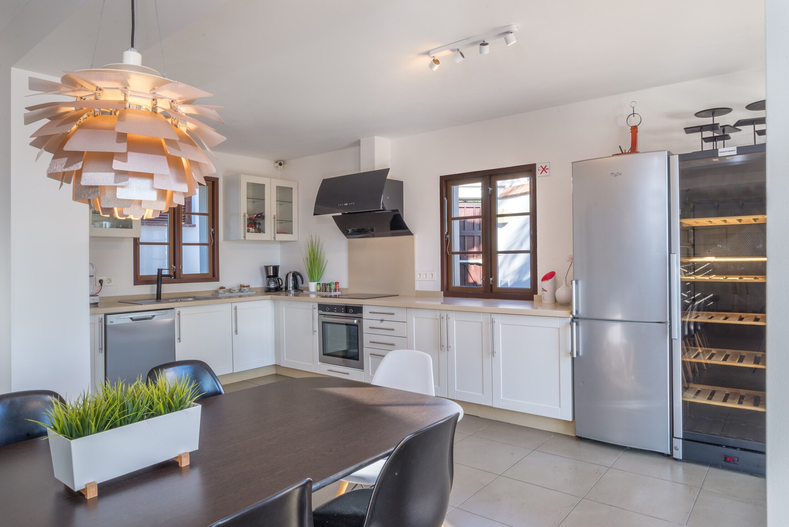 Eine moderne Küche mit weißen Schränken, einem Edelstahlkühlschrank, einem eingebauten Backofen und einer außergewöhnlichen Pendelleuchte.