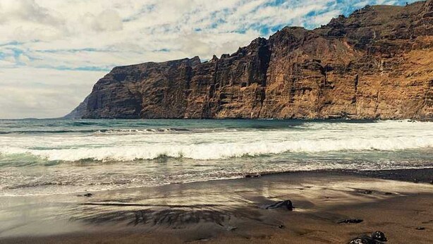 Un paysage côtier avec une falaise rocheuse et des vagues qui déferlent sur le rivage.