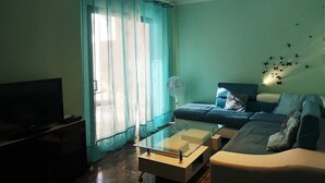 Un salon avec un canapé, une table basse en verre, un téléviseur et un ventilateur.