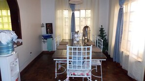 Un comedor con una mesa de madera, sillas blancas, un dispensador de agua y un objeto decorativo de metal sobre la mesa.