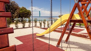 A wooden swing set with a yellow slide, located in a park with a sandy area and a view of the sea. - Mobilhome Deluxe by Interhome (Rovinj/Bale)