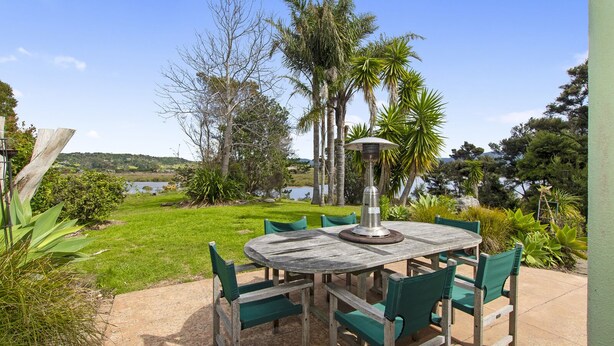 Un patio al aire libre con una mesa redonda y sillas, rodeado de follaje y vistas a un lago.