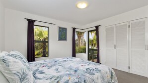 Un dormitorio con cama, ventana con cortinas, puerta y vistas al exterior.