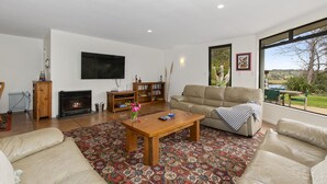 Una sala de estar con chimenea, sofá, mesa de centro y un ventanal con vistas al verdor.