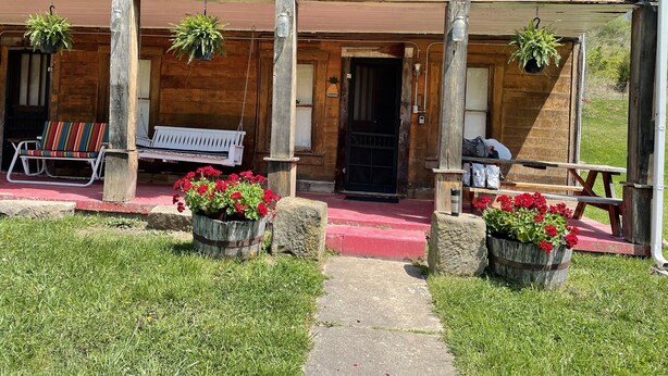 A wooden building with a balcony, a bench, and potted plants. - Rustic and Romantic Farm House (Louisa)