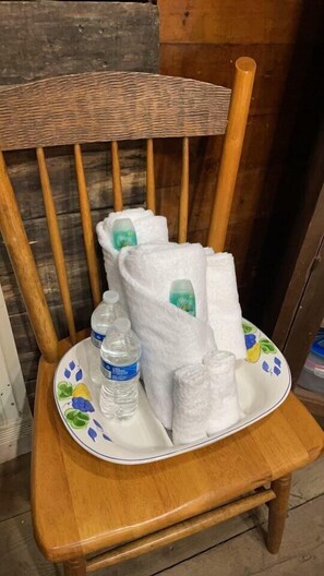 En trästol med ett brickbord som innehåller vita handdukar, en vattenflaska och en tallrik med ett fruktmotiv.