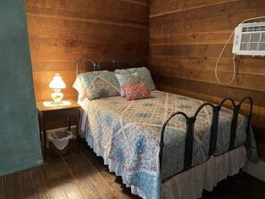 Ett rum med träpanel på väggarna, en säng, ett nattduksbord med en lampa och en väggmonterad luftkonditioneringsanläggning.
