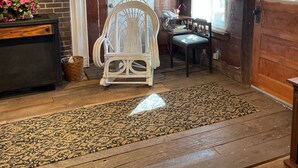 A cozy room with a wooden ceiling, a white chair, a patterned rug, and a fireplace with a framed portrait above it. - Rustic and Romantic Farm House (Louisa)