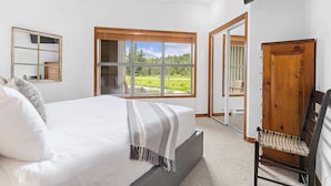Un dormitorio con una cama grande, un ventanal con vistas a un paisaje verde, una puerta de madera y una silla.