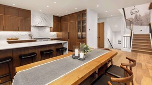 A modern kitchen with wooden cabinets, a marble backsplash, and a dining area with a long wooden table and chairs.