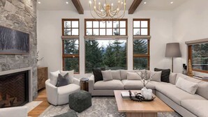 A spacious living room with a fireplace, large windows, a chandelier, and a modern sofa set.
