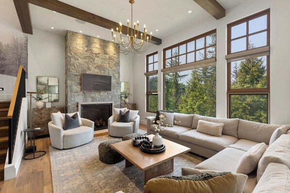 A spacious living room with a stone fireplace, large windows, and a chandelier.
