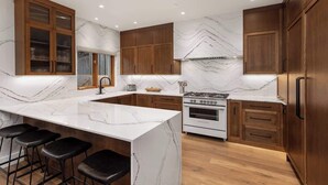A modern kitchen with marble countertops, wooden cabinets, and a central island with bar stools.