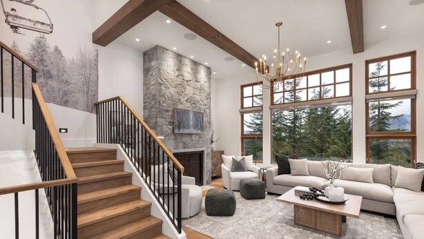 A spacious living area with a fireplace, large windows, and a staircase with wooden railings.