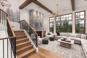 A spacious living area with a fireplace, large windows, and a staircase with wooden railings.