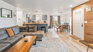 A modern living room with a sofa, coffee table, and a dining area with a table and chairs. - Walk to Downtown Sisters - DOG Friendly - Updated! (Sisters)