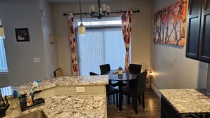 A compact kitchen with granite countertops, a dining area with a table and chairs, and a large window with curtains. - Cute & Cozy 3 BdRm, 2 1/2 Bath Townhome (Evans)