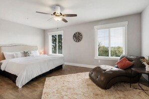 Un dormitorio con cama, ventilador de techo, reloj y ventanas amplias.