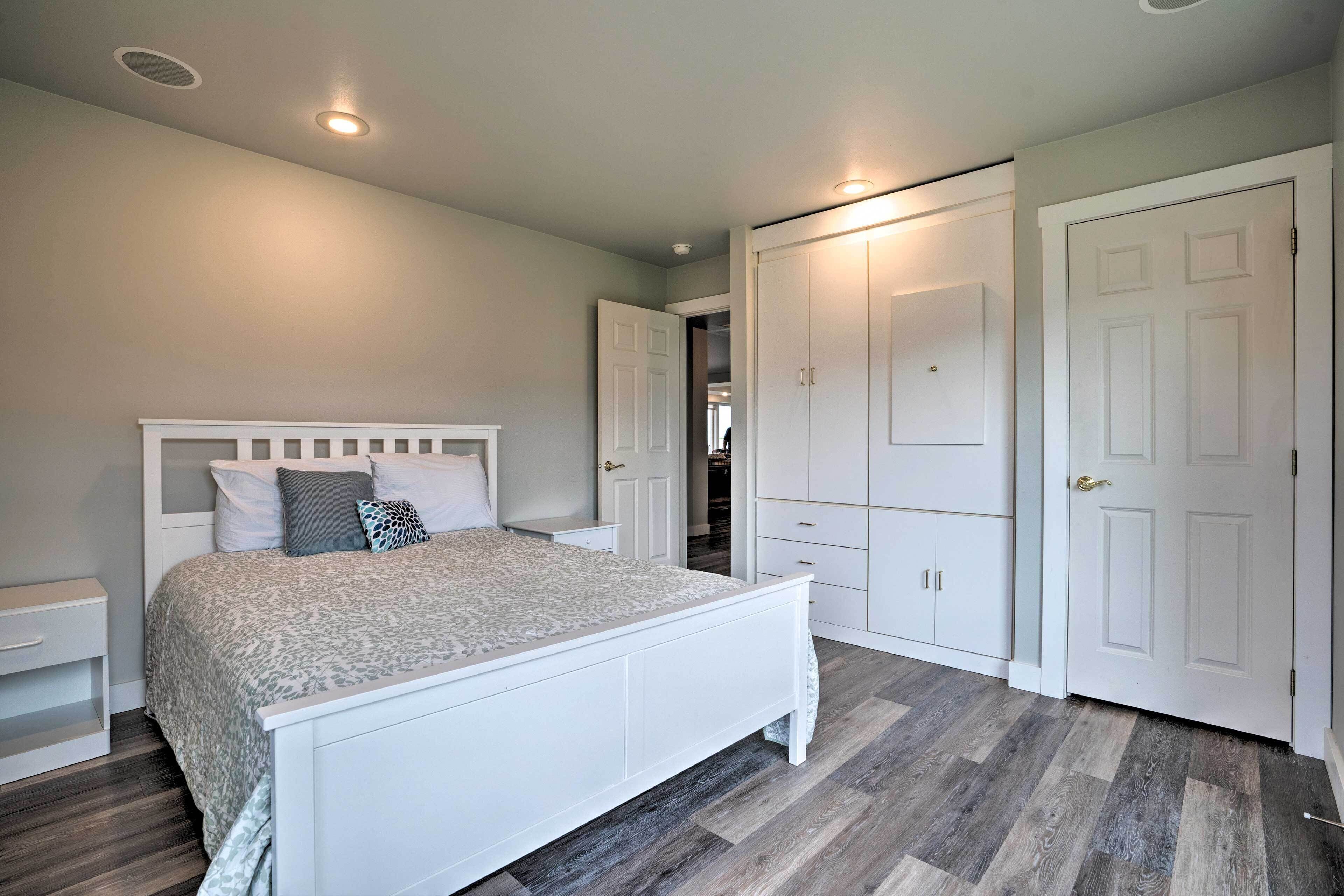 Quarto com uma cama branca, mesa de cabeceira, guarda-roupa e porta.