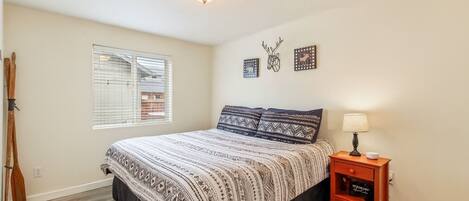 A bedroom with a bed, a nightstand, a lamp, and a window with blinds.