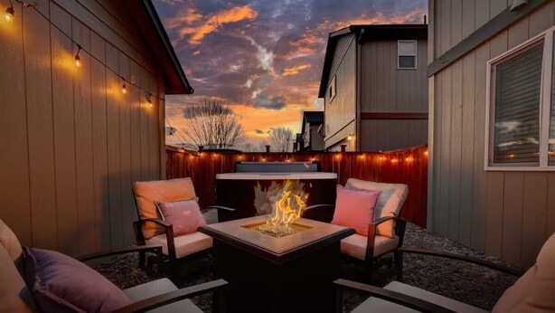 Un área de estar al aire libre con una chimenea, rodeada de paredes de madera y luces colgantes.