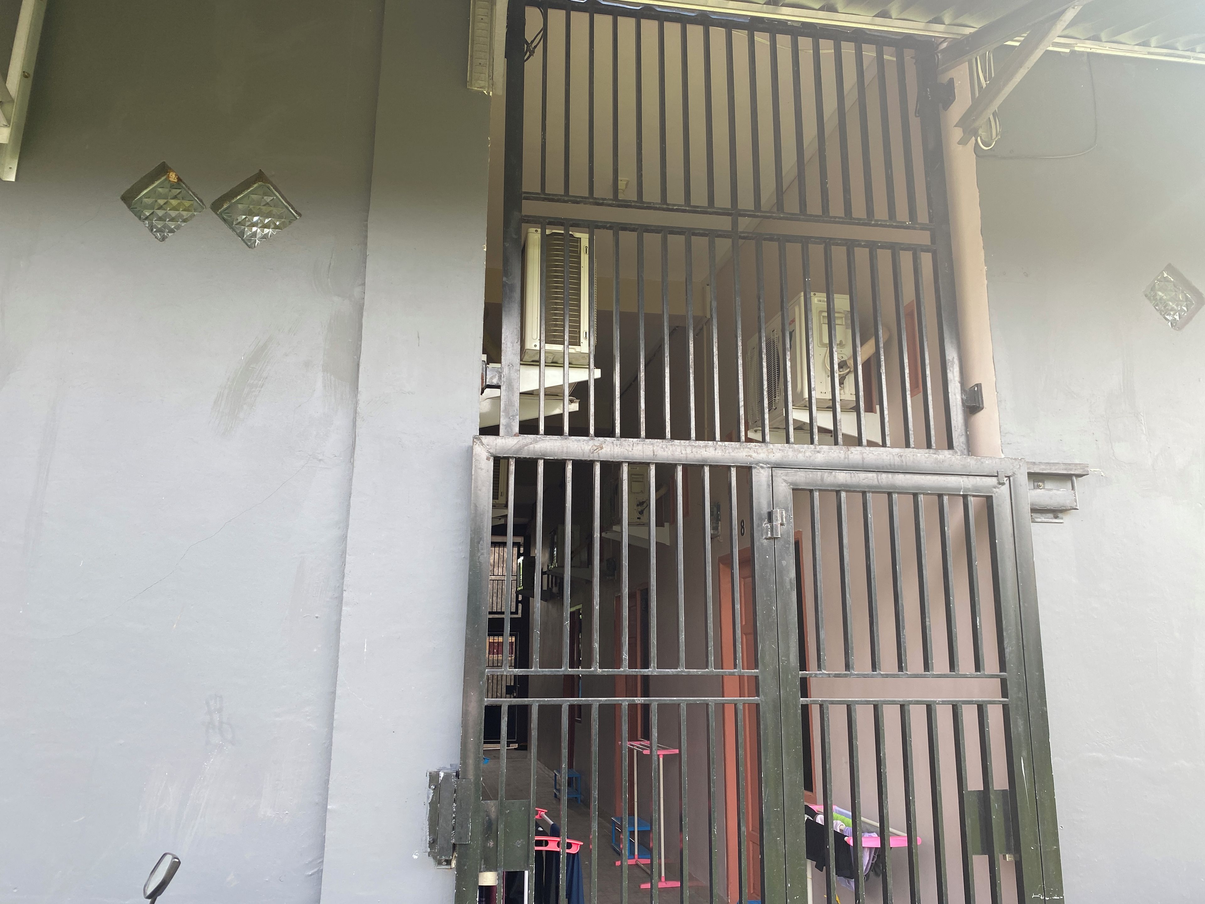 A metal gate with vertical bars, a wall with a window, and a door with a lock.