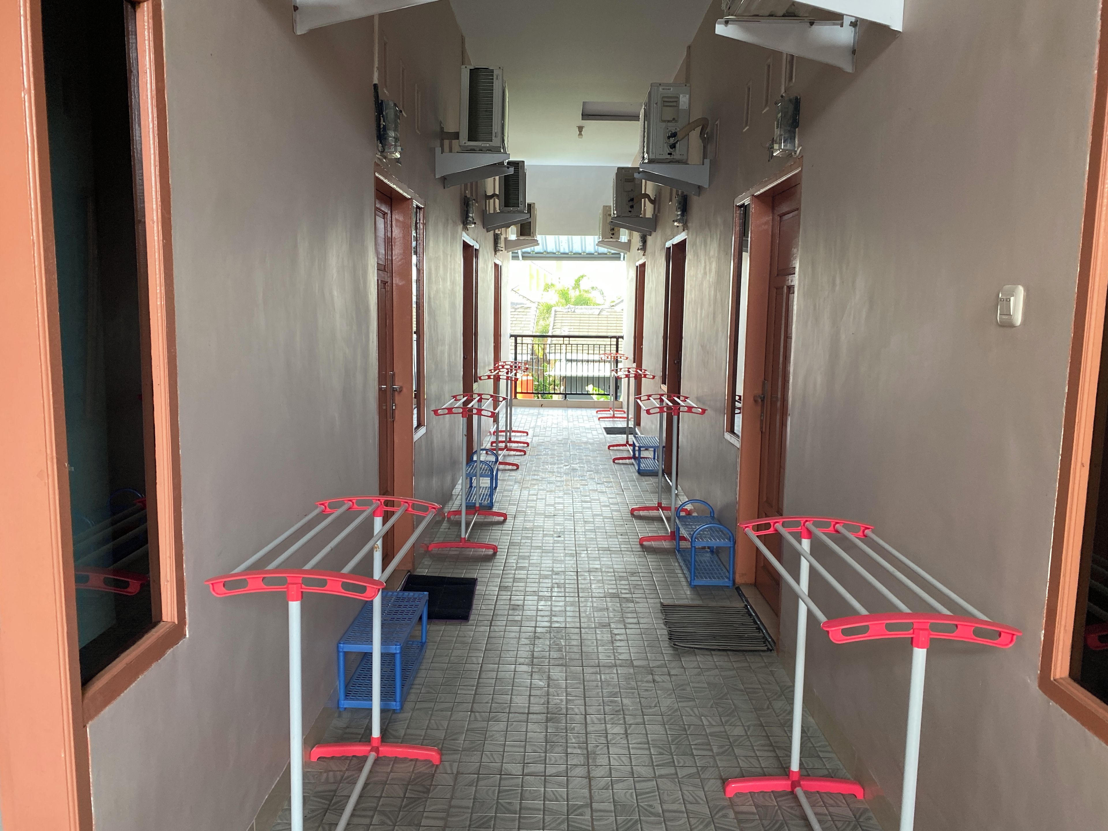 A corridor with air conditioning units, doors, and laundry racks.