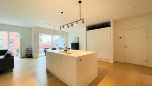 Een moderne keuken met een centraal eiland, hangende verlichting en een uitzicht op de stad door grote ramen.