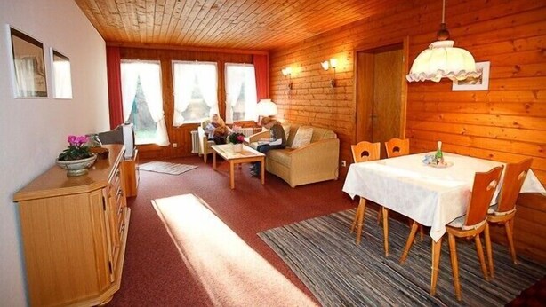 A cozy cabin interior with a wooden ceiling, a dining area with a table and chairs, a sofa, and a small kitchen area. - Fewo 3E Terr., Kochnische, 1 Schlaf- und 1 Wohn-/schlafzimmer, max 4 Pers (Ruhpolding)