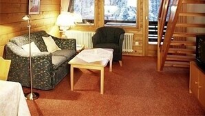 A cozy cabin interior with a sofa, a table, a lamp, and a view of snowy trees through large windows. - Fewo 3E Terr., Kochnische, 1 Schlaf- und 1 Wohn-/schlafzimmer, max 4 Pers (Ruhpolding)