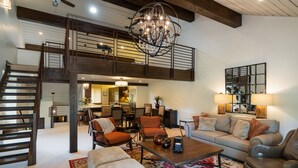 A spacious living area with a high ceiling, a chandelier, and a staircase leading to an upper level.