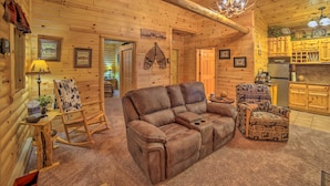 Un acogedor interior de cabaña de madera con un sofá de cuero, un sillón mecedor y un sillón estampado.