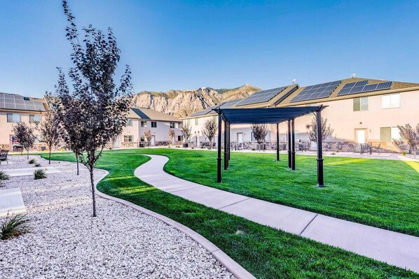 A residential area with a covered outdoor seating area, a well-maintained lawn, and a building with solar panels.