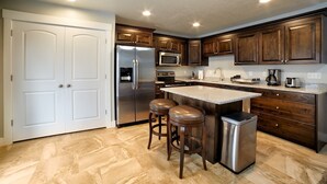 Una cocina con armarios de madera oscura, electrodomésticos de acero inoxidable y encimera de granito, además de dos taburetes.
