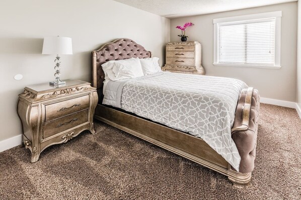 A bedroom with a bed, nightstand, dresser, and a window with blinds.