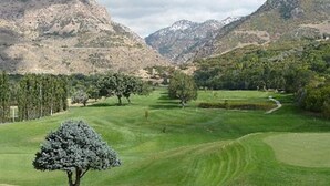 Un campo de golf con un césped cuidado, árboles y montañas al fondo.