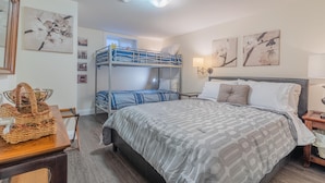 A bedroom with a bunk bed, a large bed with patterned bedding, a wooden desk with a basket, and wall-mounted artwork.
