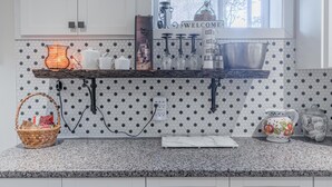 A kitchen with white cabinets, a granite countertop, a window with a 'WELCOME' sign, and a hexagonal tile backsplash.