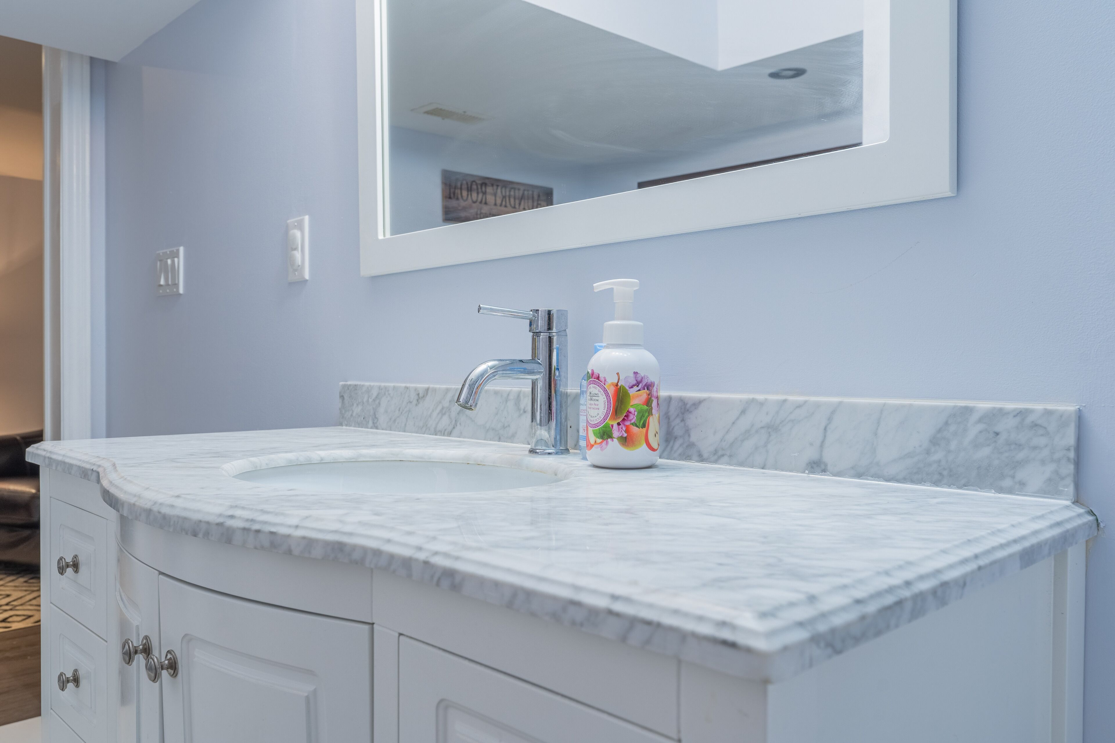 A bathroom with a marble sink, a mirror, and a bottle of hand soap.